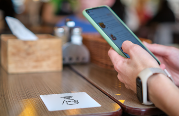 A smartphone gently tapping an NFC sticker embedded with a microchip, showcasing the application of near field communication stickers in mobile interaction and business operations.