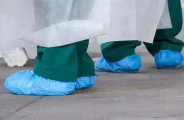 Medical staff wearing protective gowns, green scrubs, and blue disposable shoe covers for hospital infection control and hygiene compliance