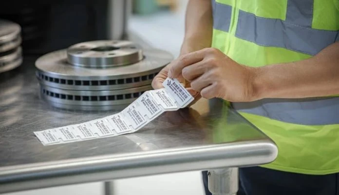 On-Metal RFID Label A worker peeling an anti-metal RFID label from a roll on a stainless steel workstation next to metal mechanical parts