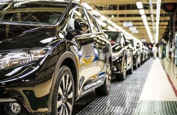 A row of finished black cars lined up along an automotive assembly line in a factory.