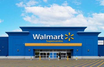 The exterior front entrance of a bright blue Walmart Supercentre retail store under a cloudy blue sky.