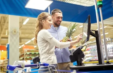 Self-checkout at Store A couple using a self-checkout kiosk in a store with a pineapple.