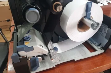 A close up view of an RFID tag printer with a roll of blank labels being loaded for printing.