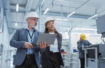 Two professionals in helmets discussing work with a laptop in an industrial setting