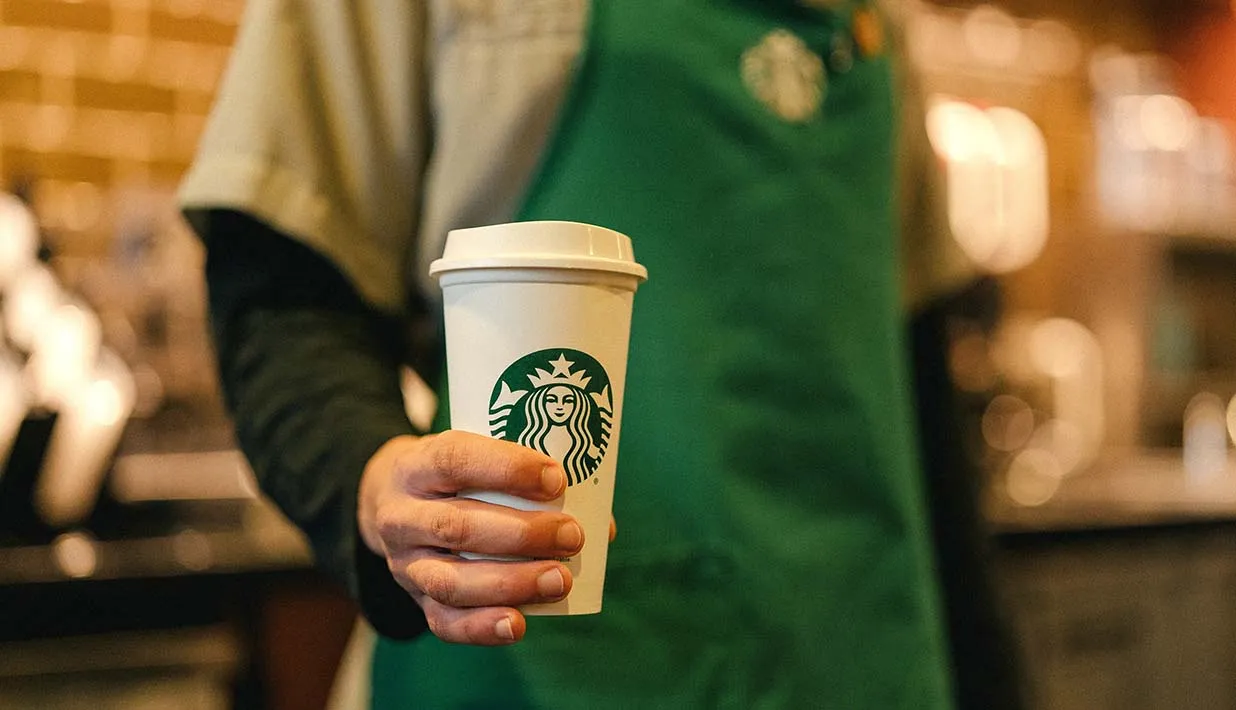 A Starbucks employee holding a cup of coffee.