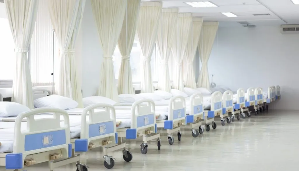 Hospital ward with empty beds and white curtains.
