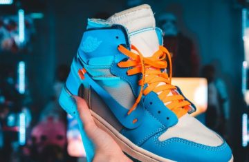 A hand holding a bright blue sneaker with orange laces and a white base