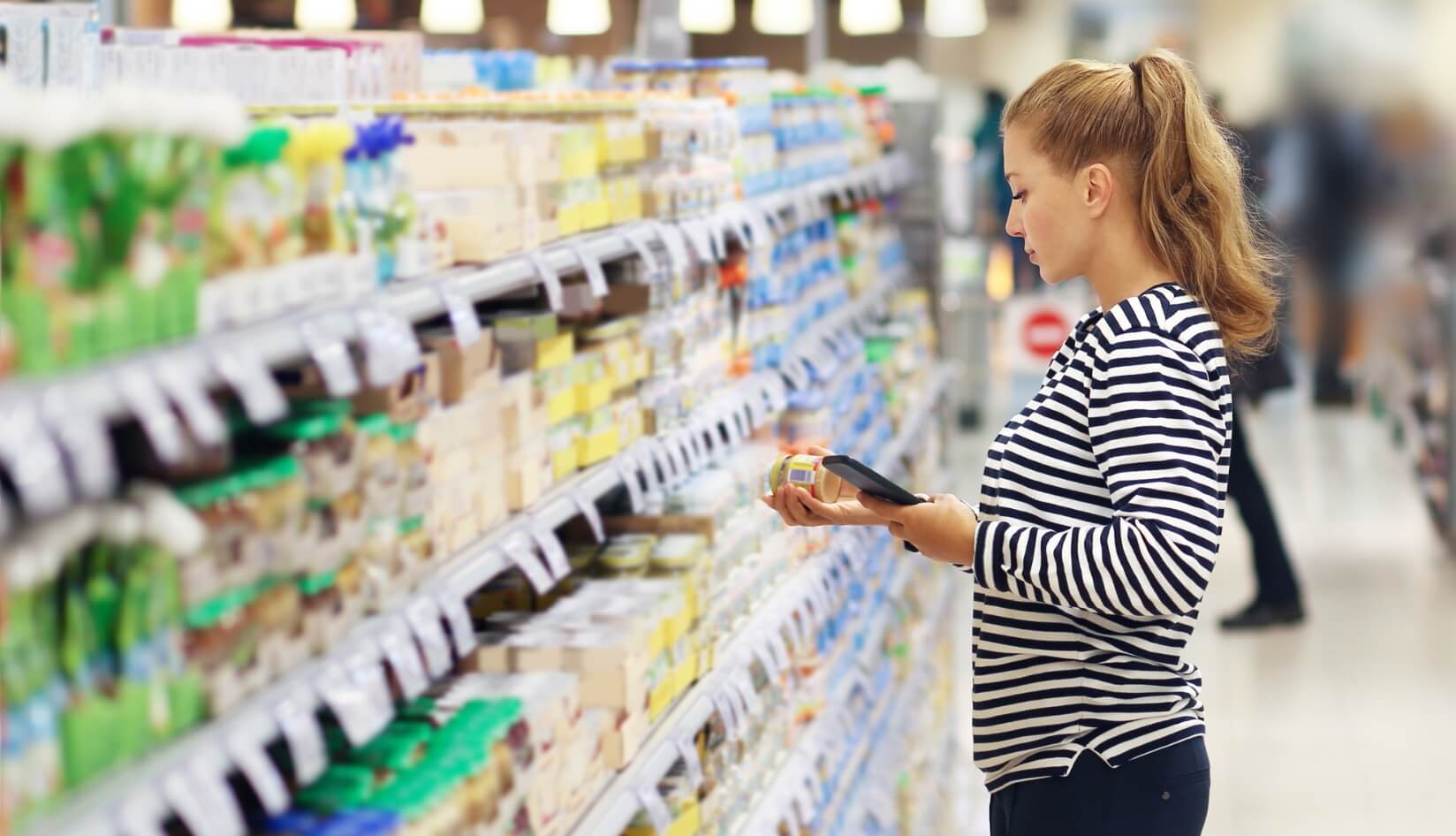 Shopper Scanning Product in Supermarket Aisle Woman using a smartphone to scan a product in a supermarket aisle full of food products.