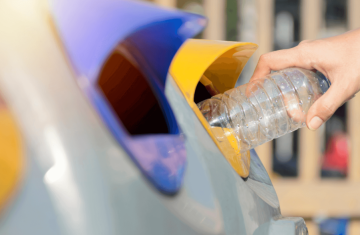 A person placing a plastic bottle into a recycling bin with multiple color-coded openings.
