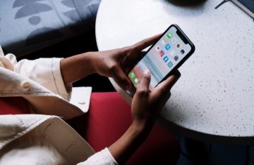 Person holding a smartphone with various apps visible on the screen.