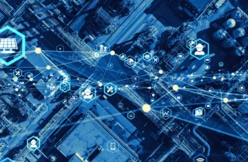 Smart Factory and Industrial Internet of Things (IIoT) An aerial view of a factory with a blue overlay of a digital network and technology icons representing smart industry.