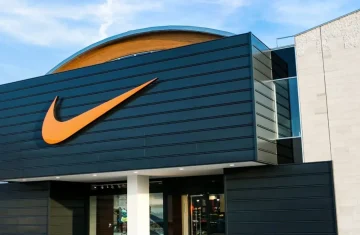 The exterior of a modern Nike retail store, featuring a large orange swoosh logo on a black paneled facade.