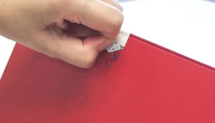 Tamper-Evident RFID Label A hand peeling a tamper-evident security sticker off a red box, leaving behind a residue pattern.