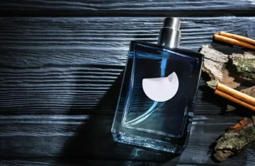 A bottle of men's cologne with a blank white label, artfully arranged on a dark wooden surface with cinnamon sticks and tree bark.
