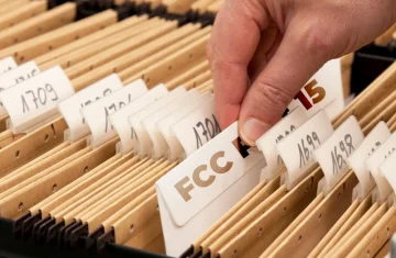 Searching for FCC Documentation A hand searching through a filing cabinet and pulling out a file labeled "FCC".