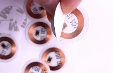 T5577 RFID Tag Peeling Process A close-up of a person peeling the protective layer from a T5577 RFID tag with a copper coil visible.