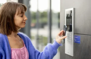 Smartphone NFC/RFID for Secure Access Control A woman using her smartphone to interact with a modern, sleek silver access control panel next to a door.