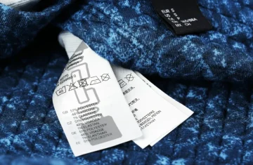 A close-up of a clothing care label showing material composition and washing instructions on a blue textured garment.