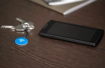 NFC Key Tag Beside Smartphone on Desk Smartphone and house keys with a blue NFC key tag lying on a wooden desk.