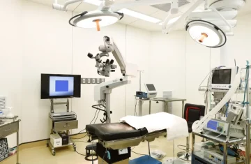 State-of-the-Art Surgical Operating Room A modern, well-equipped operating room with a surgical bed, large overhead lights, a microscope, and various monitors.