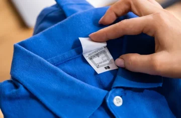 Anatomy of an RFID Tag in Apparel Care Labels A hand points to the care label of a blue polo shirt, where a small, square RFID inlay is visible within the label fabric.