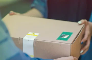 A person handing over a cardboard box with a visible RFID tag sticker on the side, used for tracking and packaging.