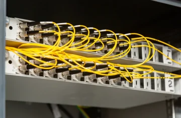 Fiber Patch Panel with Yellow Patch Cords in Rack Close-up of a network patch panel with yellow fiber optic patch cables connected to multiple ports in a rack cabinet.