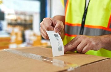 How Chip RFID Tag Adhesive Ensures Reliability in Harsh Environments Warehouse worker applying an RFID label with visible antenna to a taped cardboard shipping box.