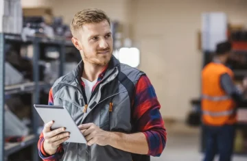 Maximize ROI and Eliminate Lease Penalties Why an RFID it asset tracking system is Your Best Investment Warehouse manager holding a tablet for inventory tracking, standing in a storage area with shelves.