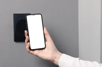 Apple NFC Opens in 2026 New Access Control Opportunities Hand holding a smartphone near a wall mounted reader for mobile access control.
