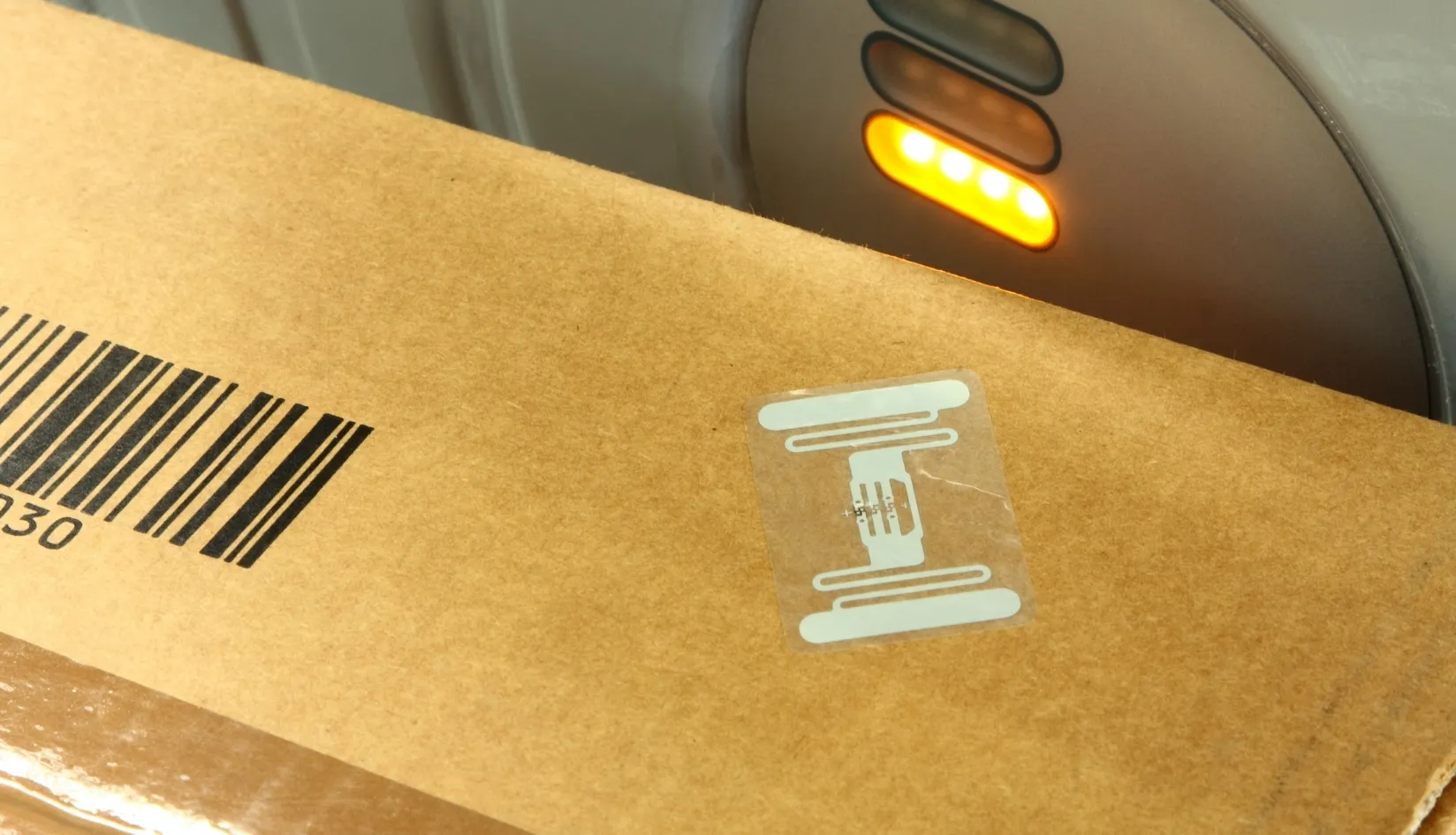 Brown package with RFID tag and barcode being scanned by a device with orange lights