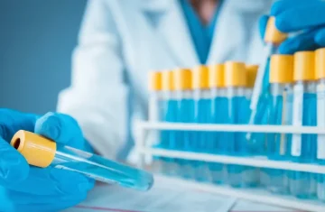 A lab worker handles test tubes with blue liquid during scientific sample analysis.