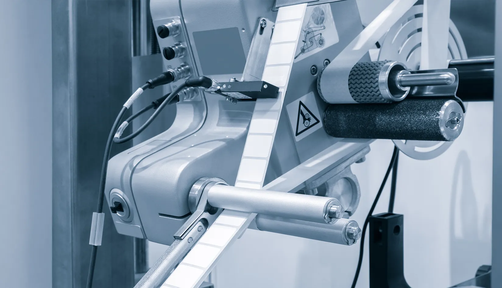 RFID Label Pitch and Gap What They Mean and Why They Matter Automated RFID label applicator feeding a roll of white labels through rollers, showing label spacing for pitch and gap control.