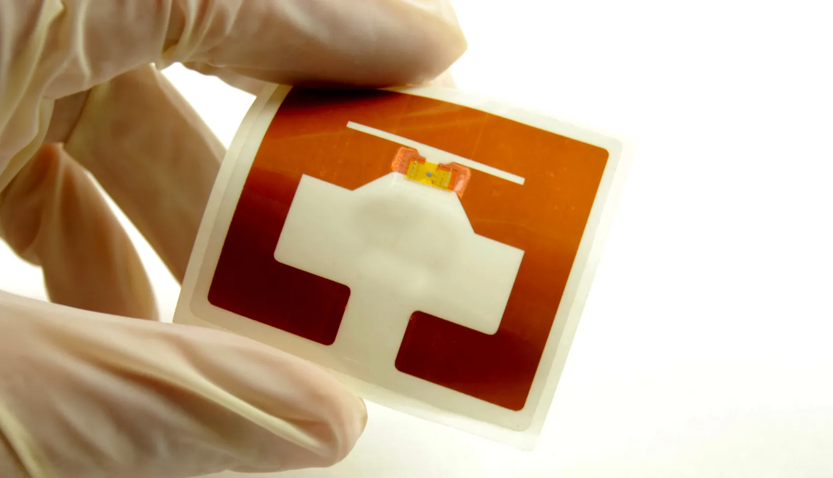 Gloved hands holding a UHF RFID inlay with chip and antenna, showing chip antenna matching for stable label performance.